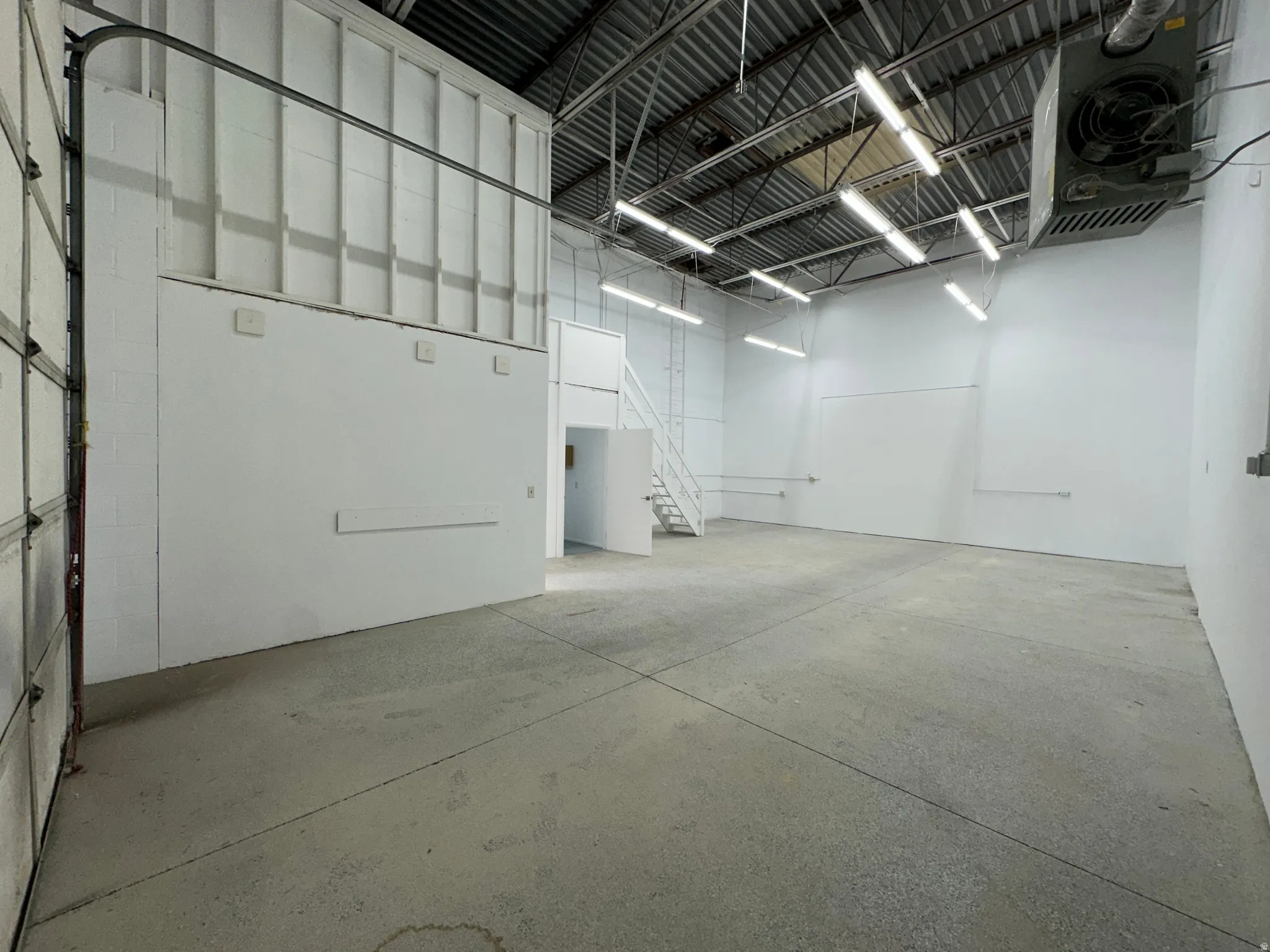 Spacious warehouse interior featuring a high ceiling, exposed metal trusses, and fluorescent lighting