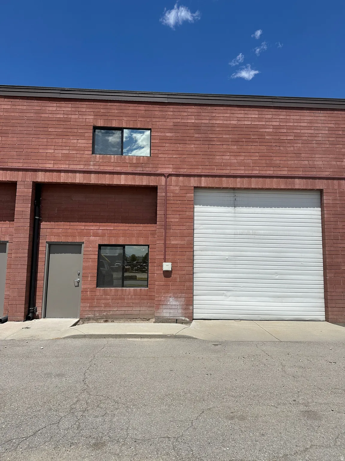 Red brick exterior featuring a roll-up garage door, a single entry door, and two distinct windows