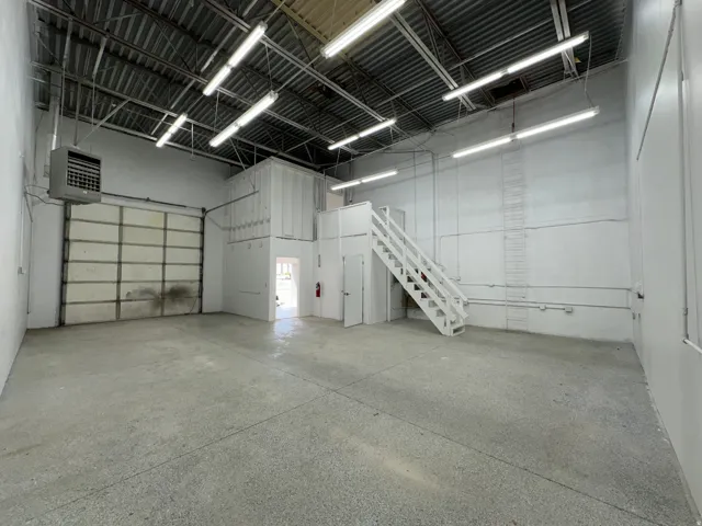 Spacious industrial interior featuring concrete flooring, a large overhead door, and exposed ceiling joists