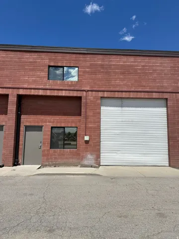 Red brick exterior featuring a roll-up garage door, a single entry door, and two distinct windows