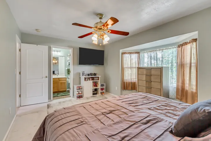 Spacious bedroom featuring light-colored walls, a ceiling fan with integrated lighting, and carpet flooring