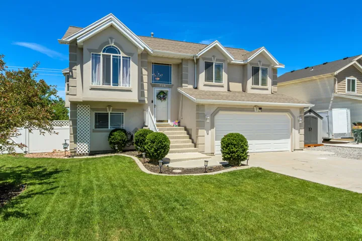 Two-story residence featuring light-colored stucco siding, dormer windows, and an attached two-car garage