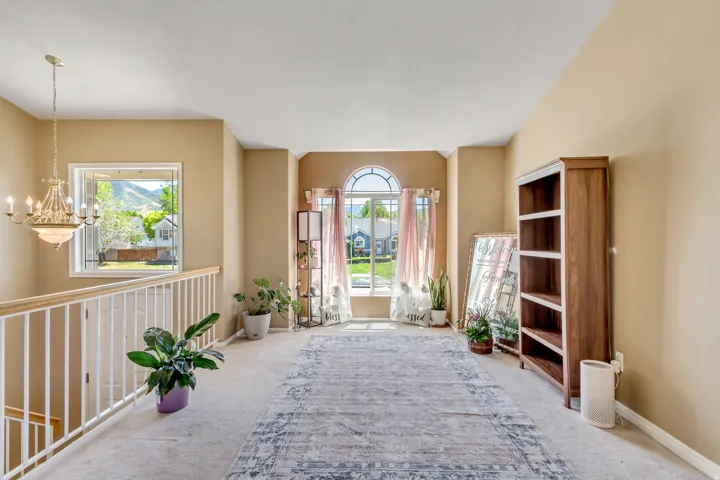 Upper-level landing featuring a large arched window, neutral carpet flooring, and a white baluster railing with a natural wood-finish handrail