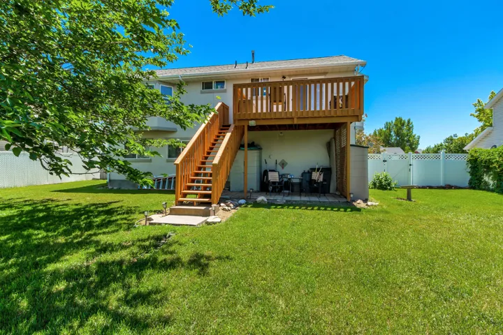 Expansive green lawn with a two-story residence featuring a wood-tone deck and matching staircase
