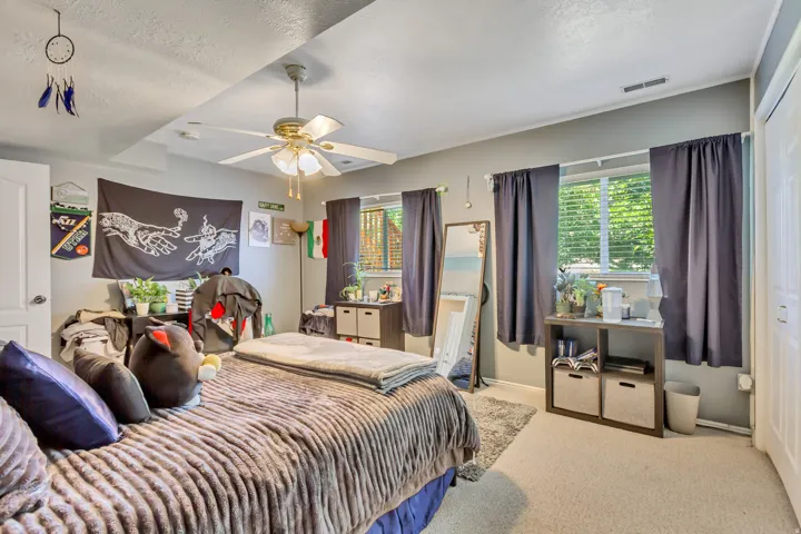 Carpeted room featuring a ceiling fan with integrated lighting, two windows with blinds, a white door, and a built-in closet with a white bi-fold door