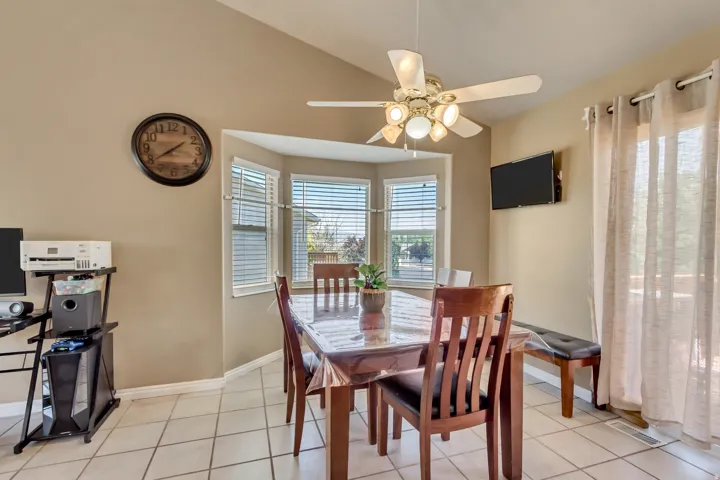 Dining area featuring a vaulted ceiling with a ceiling fan, a bay window with blinds, and white square tile flooring