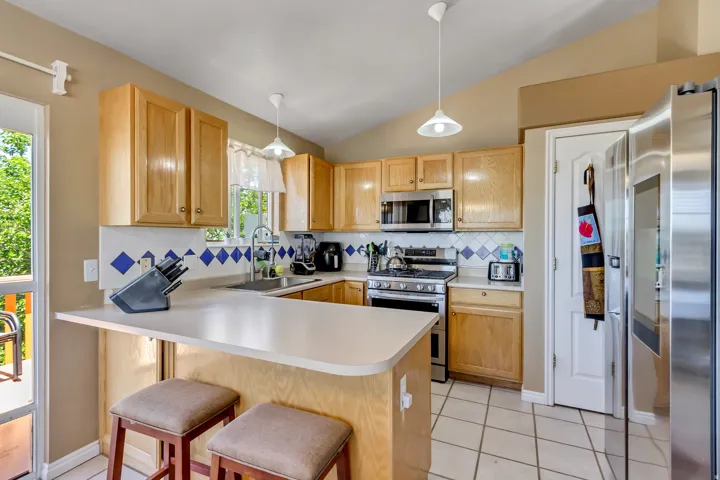 Full kitchen with wood cabinetry, stainless steel appliances, ceramic tile flooring, and a breakfast bar