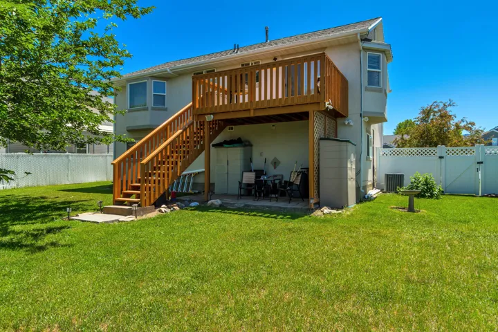 Expansive grassy backyard featuring a multi-level deck with wooden railings, an outdoor patio beneath the upper deck, and white vinyl fencing enclosing the property
