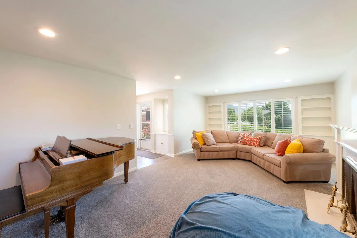 Spacious living area featuring neutral carpet flooring, recessed lighting, and a large window with white plantation shutters