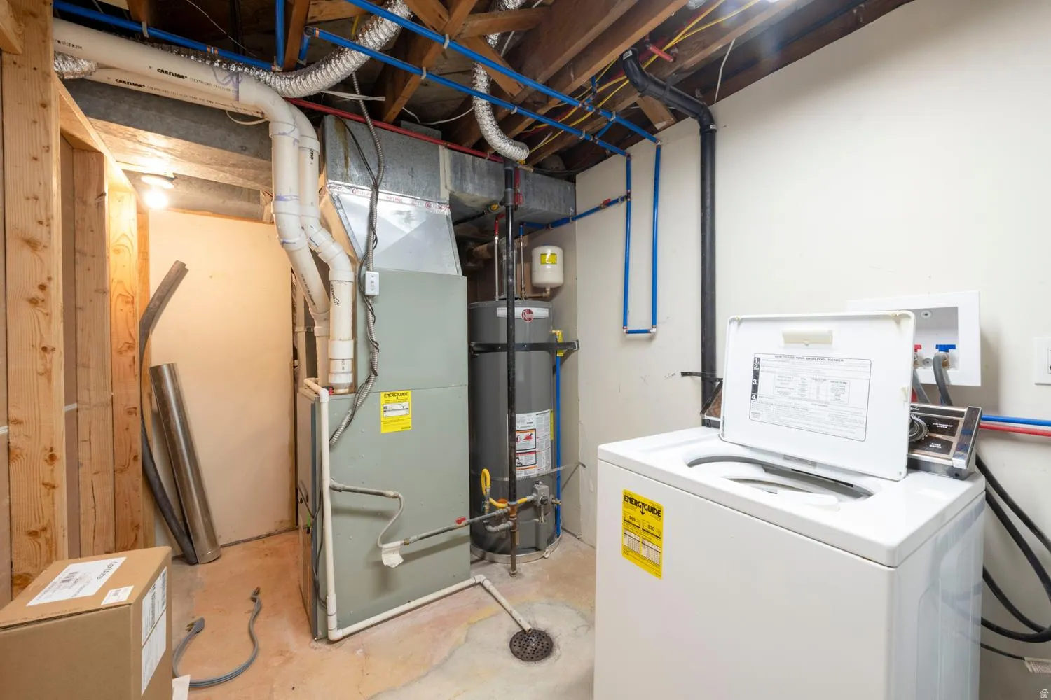 Utility room featuring exposed ceiling joists, white painted walls, a large furnace unit, a water heater, and PEX plumbing lines