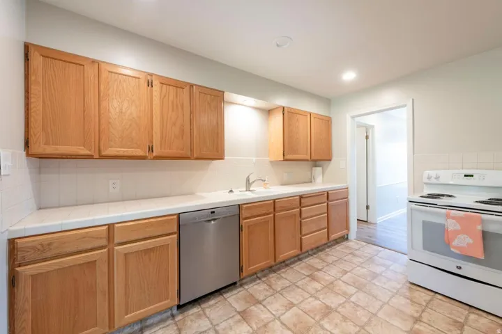 Kitchen featuring cabinetry, white countertops, tile backsplash, stainless steel dishwasher, and white electric range