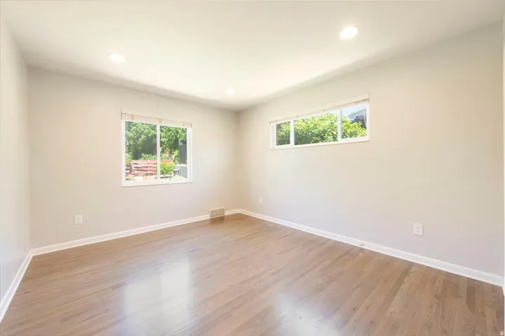 Spacious room featuring light wood-finish flooring, recessed lighting, and two windows providing ample natural illumination