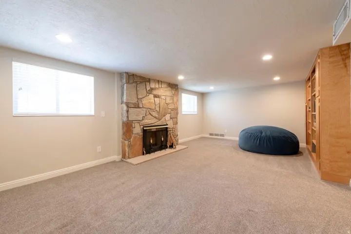 Spacious family room featuring a stone-faced fireplac, light-colored carpeting, recessed lighting, and a built-in wood-finish shelving unit