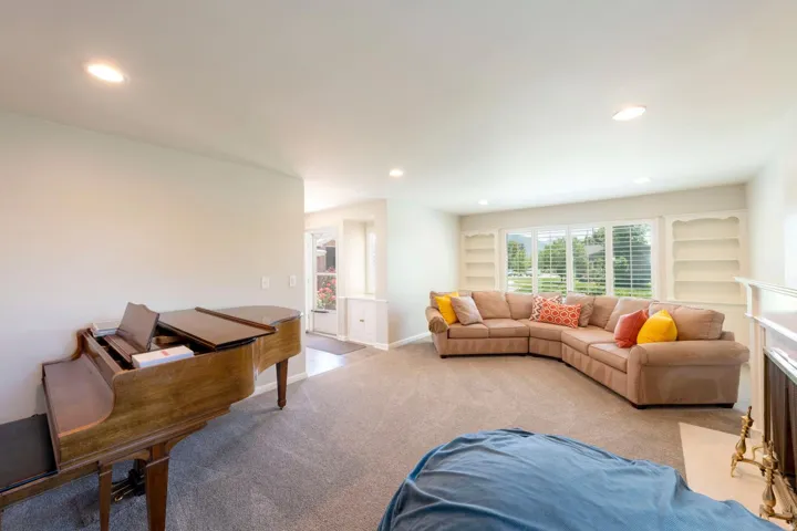 Spacious living area featuring neutral carpet flooring, recessed lighting, and a large window with white plantation shutters