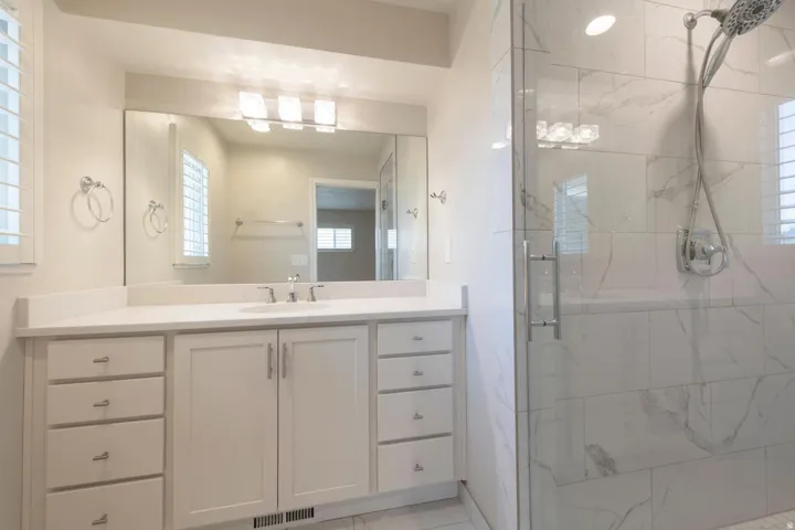 Primary bathroom featuring a glass-enclosed shower with large format tile, a white vanity with extensive storage, a single basin sink, and a large mirror with integrated lighting
