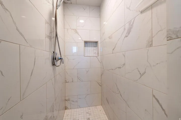 Walk-in shower featuring large format white and grey veined tile, a mosaic tile floor, and a recessed niche