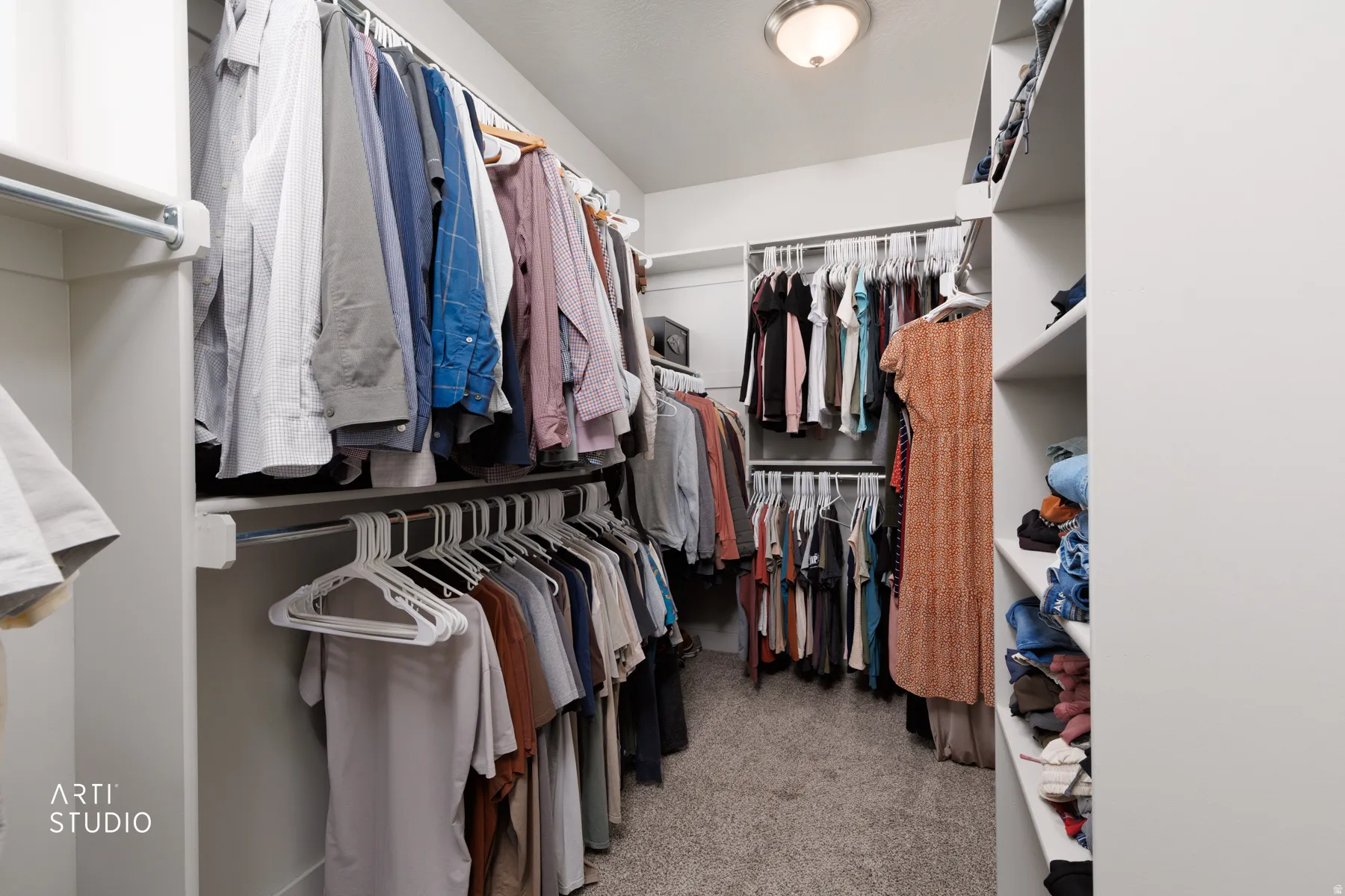 Walk-in closet with carpet flooring, custom shelving, multiple hanging rods, and an overhead flush-mount light fixture