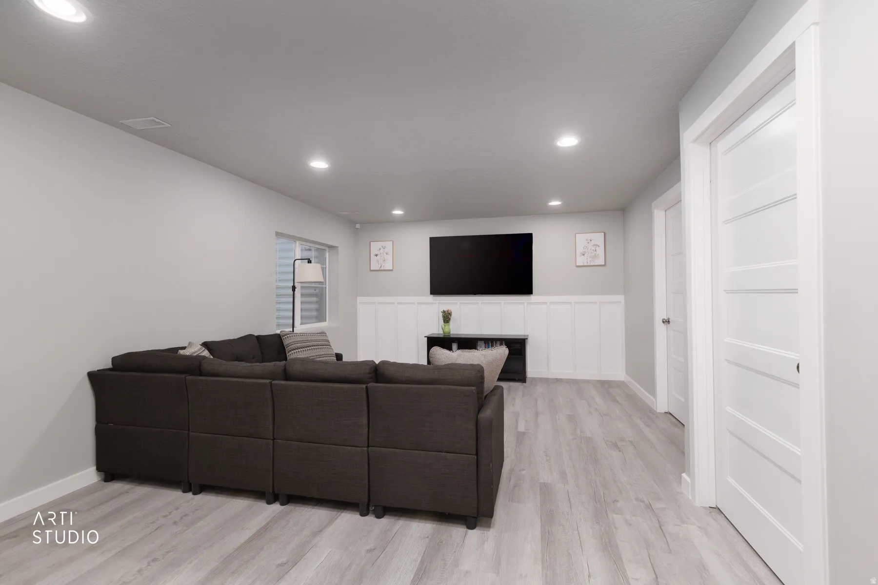 Spacious room featuring light wood-finish flooring, recessed lighting, and a white wainscoting accent wall