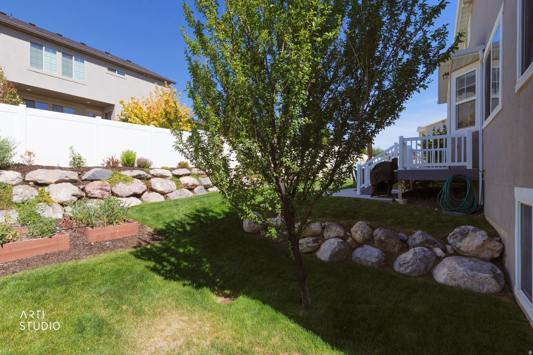 Expansive backyard featuring a manicured lawn, a large rock retaining wall, and two raised garden beds