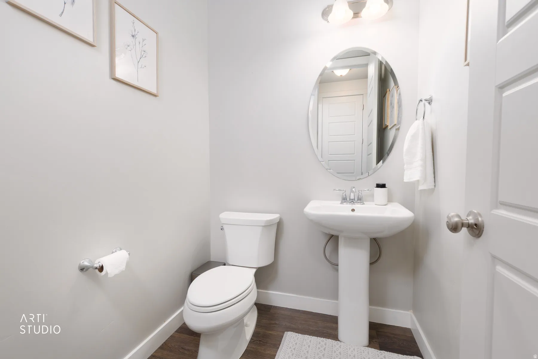 Pedestal sink with chrome faucet, oval mirror, and overhead vanity lighting
