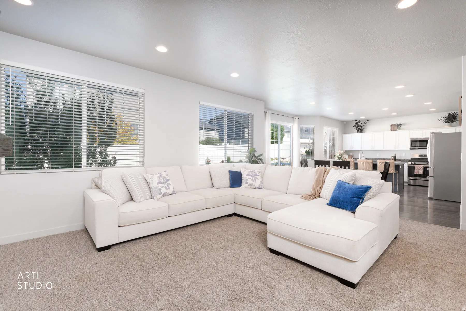 Open-concept living area featuring recessed lighting, light-toned carpeting, and multiple windows with blinds