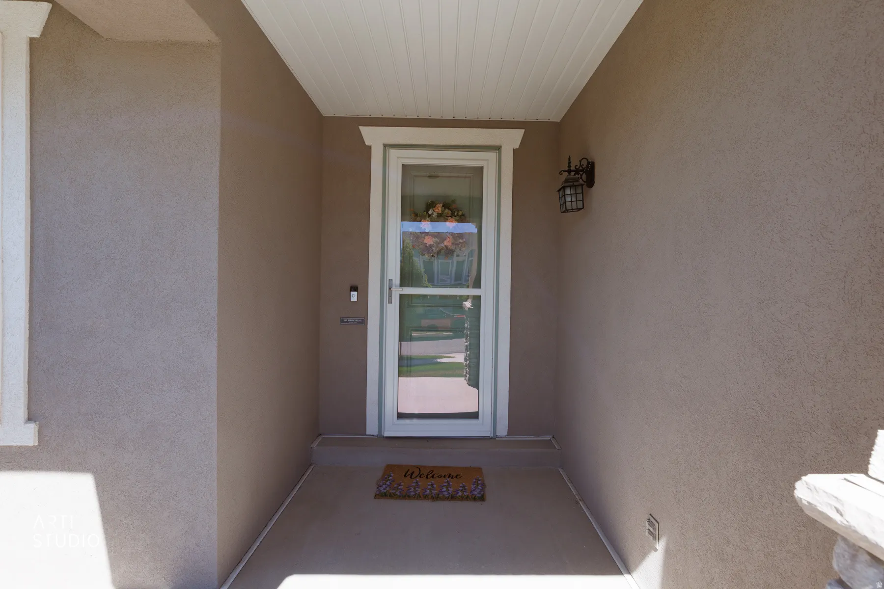 Recessed entry featuring stucco walls, a beadboard ceiling, white trim accents, and an exterior wall lantern