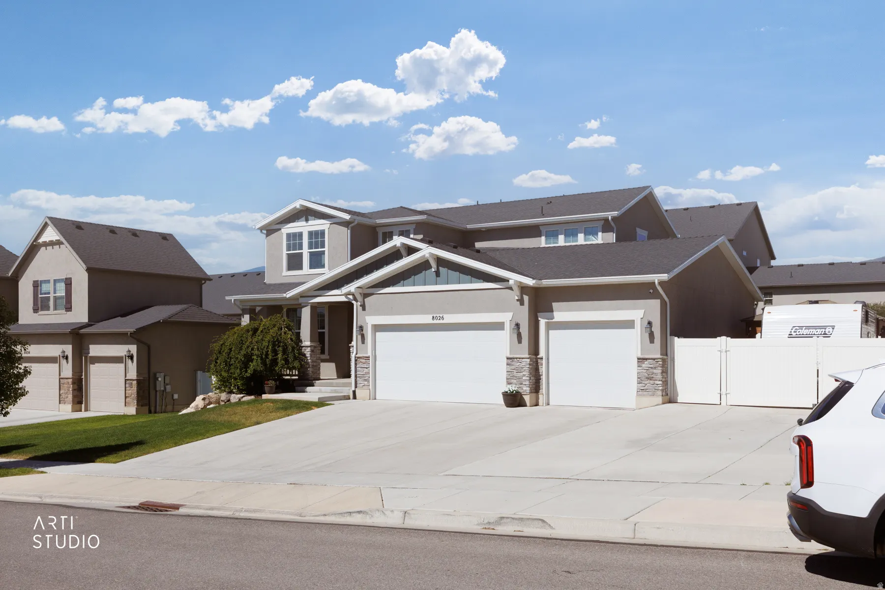 Contemporary stucco exterior with stone accents, a multi-car driveway, attached two-car garage, and a privacy fence