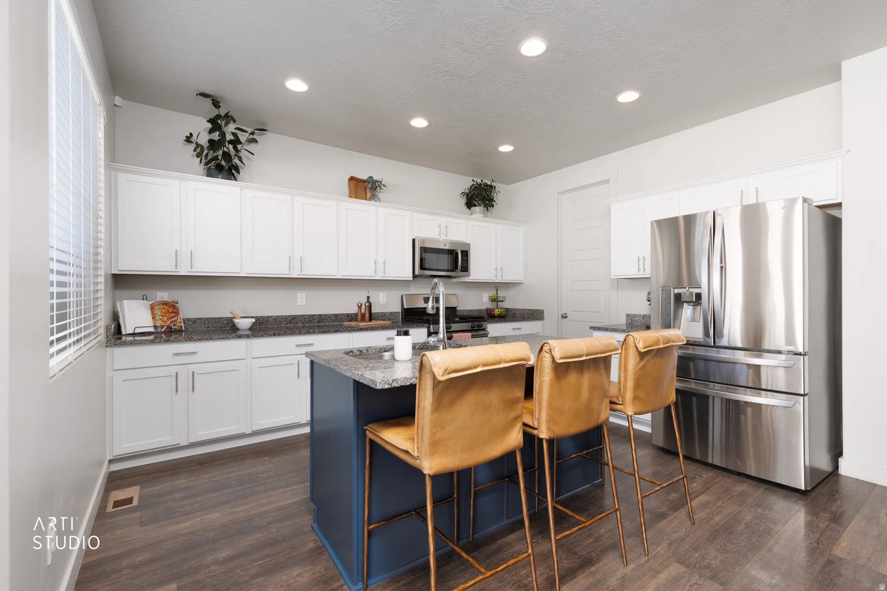 Contemporary kitchen featuring a dark blue island, white upper and lower cabinetry, stainless steel appliances, wood-finish flooring, and recessed lighting