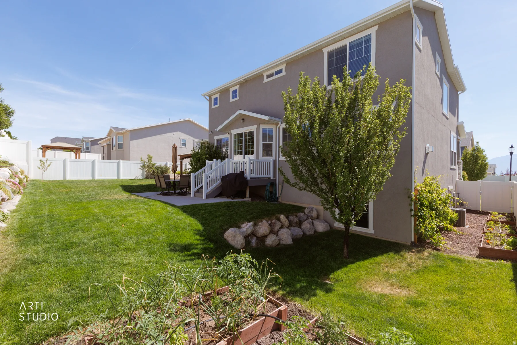 Expansive backyard featuring a manicured lawn, a concrete patio, and a white vinyl fence