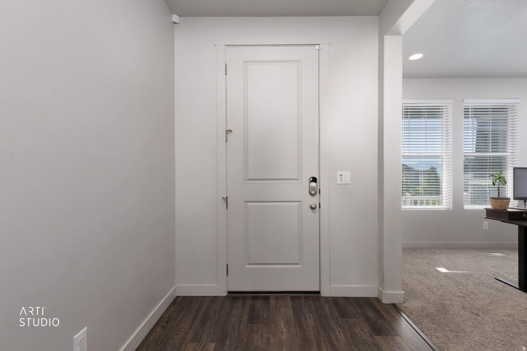 Entryway featuring a white paneled door with smart lock hardware, wood-finish flooring, and a broad archway opening to an interior space with large windows
