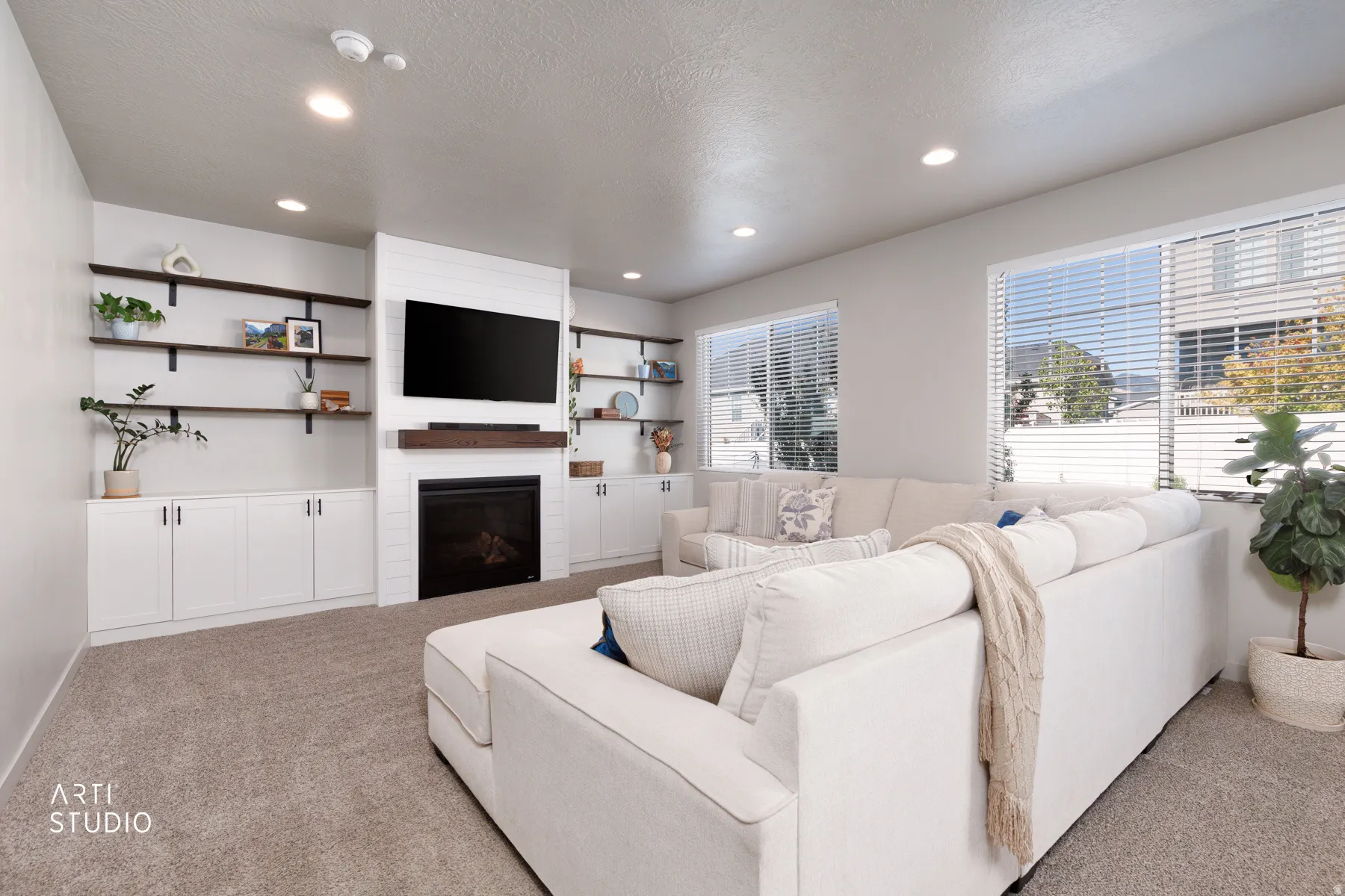 Living area featuring a shiplap fireplace with a wood mantel, built-in white cabinetry, open wood shelving, recessed lighting, and carpet flooring