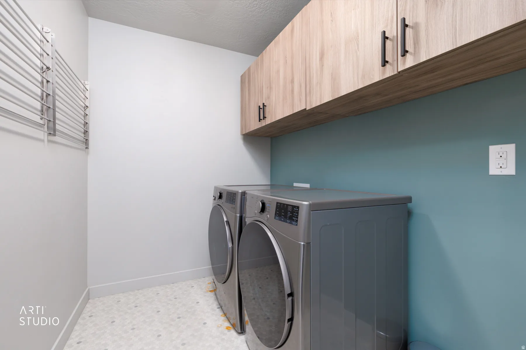 Laundry area featuring wood-finish cabinetry with matte black hardware, a teal accent wall, and patterned floor tiling