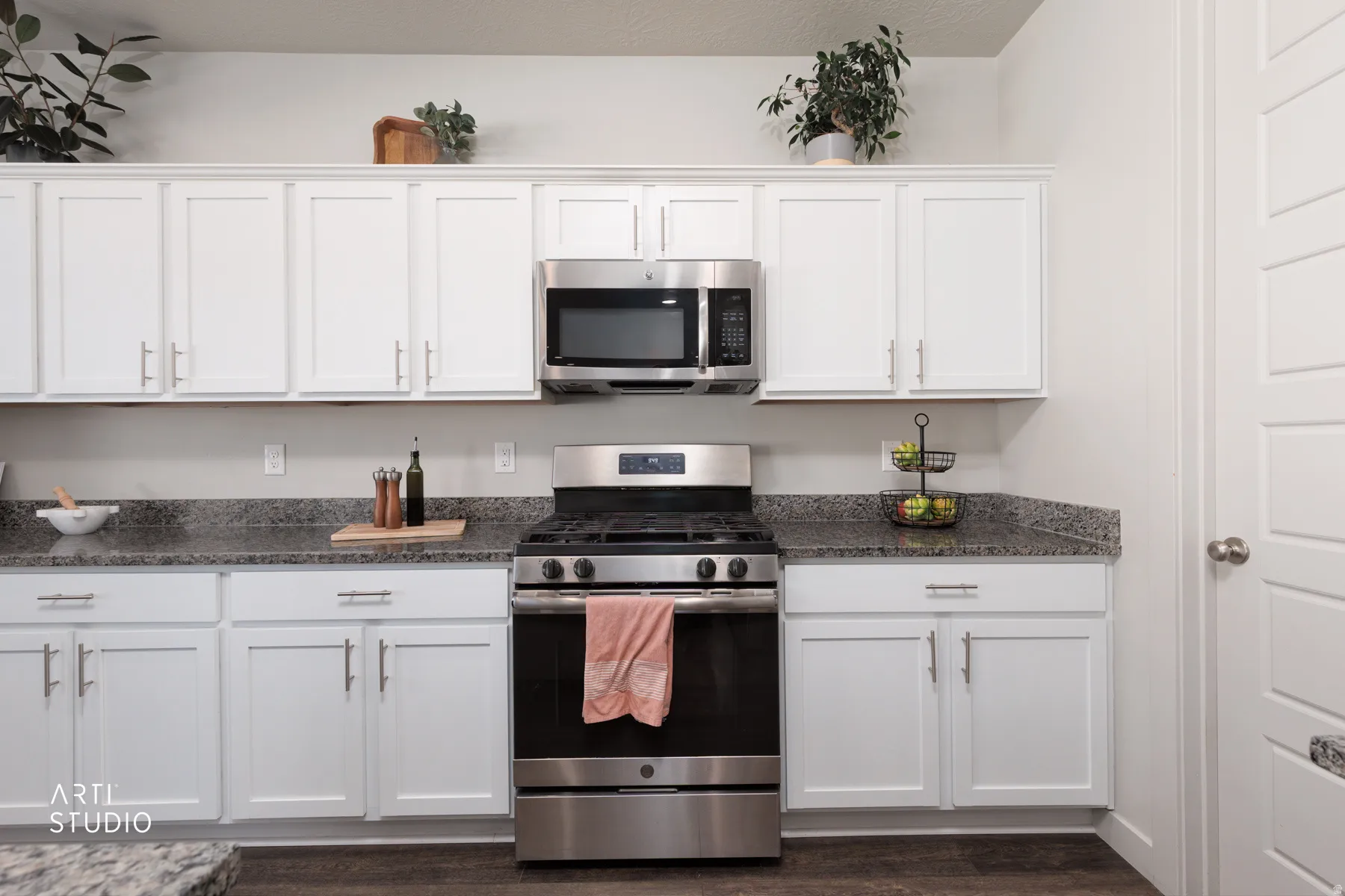 Modern kitchen featuring white shaker cabinetry, stainless steel appliances, speckled stone countertops, and wood-finish flooring