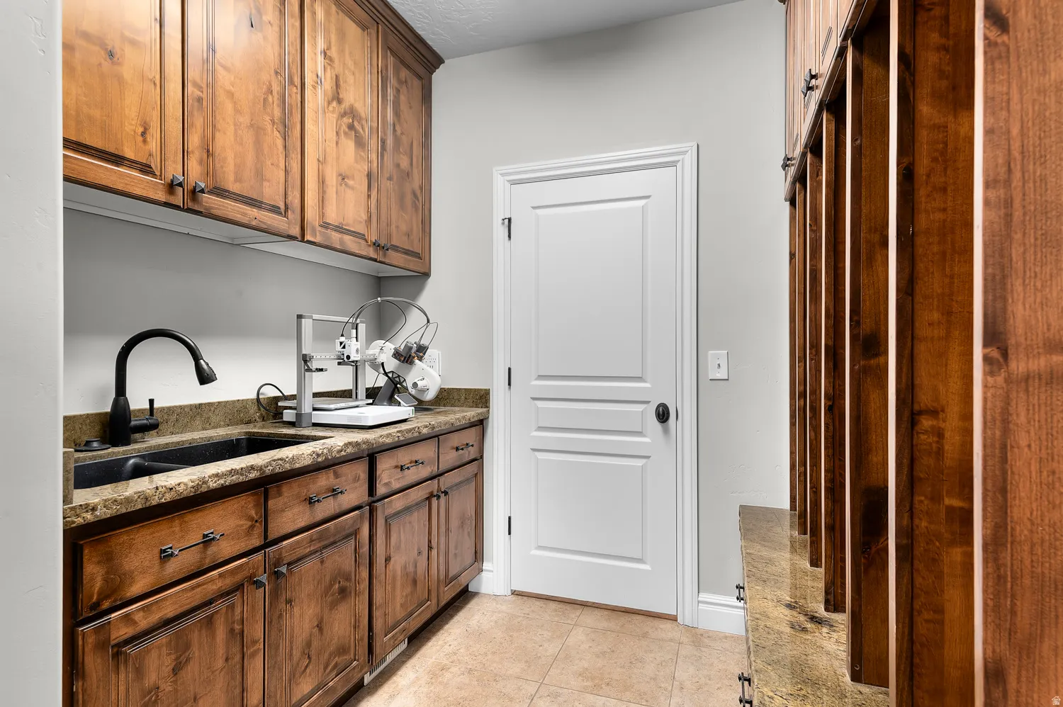 Utility space featuring wood-finish cabinetry, a black undermount sink, and a black gooseneck faucet