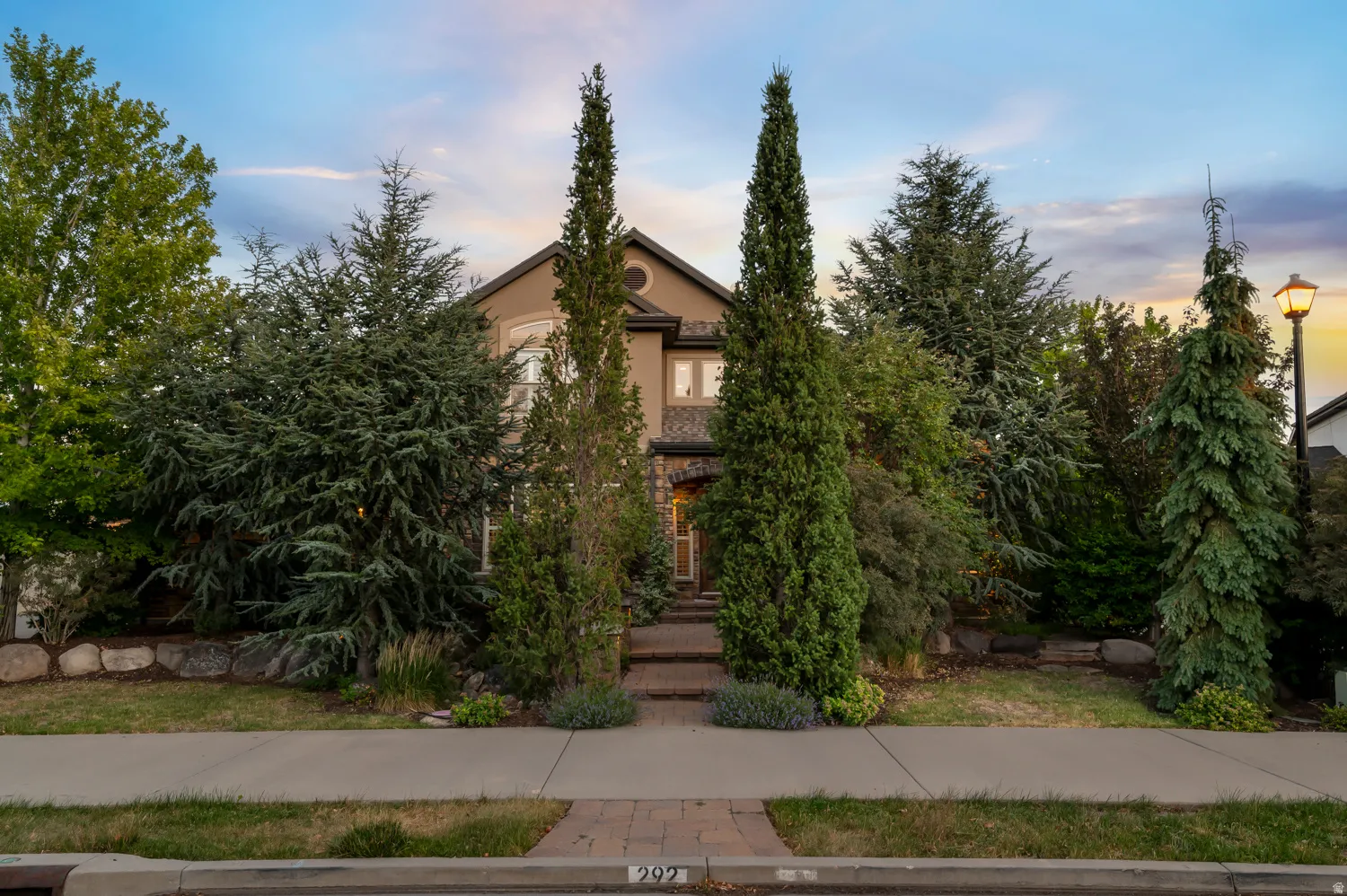Stucco exterior with stone accents and mature evergreen landscaping