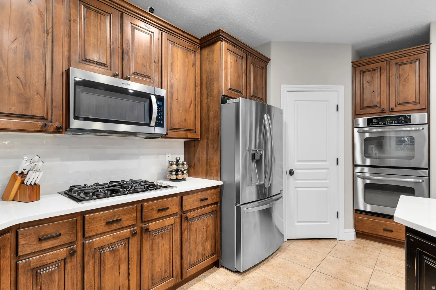 Gourmet kitchen featuring rich wood cabinetry, stainless steel appliances, a gas cooktop, white subway tile backsplash, and light-toned countertops