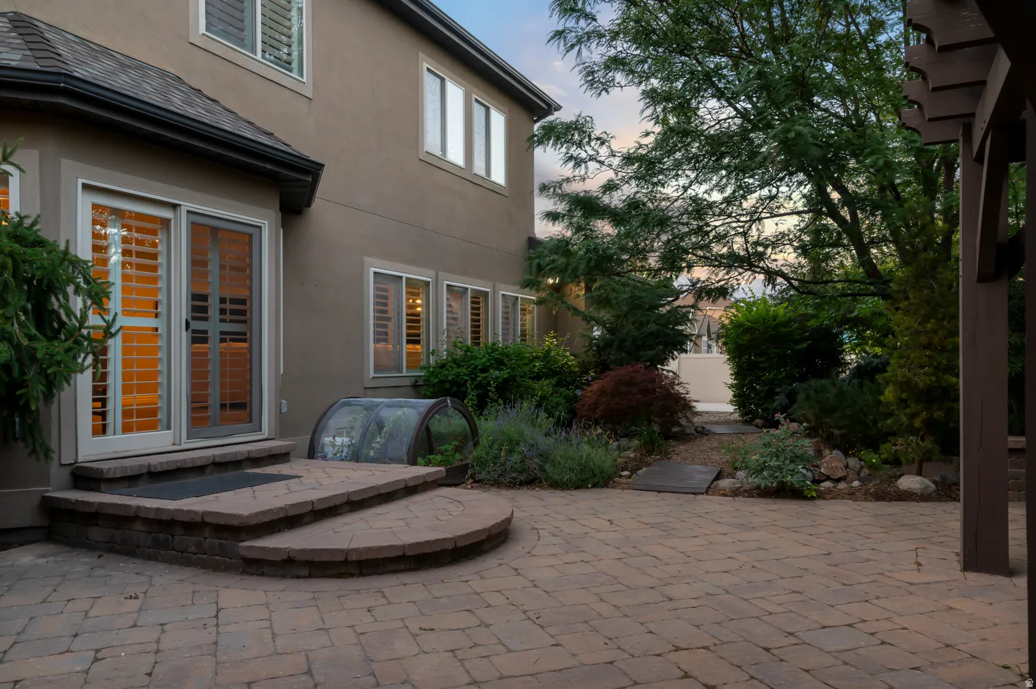 Spacious paver patio with a curved brick step-up, surrounded by mature trees and varied landscaping