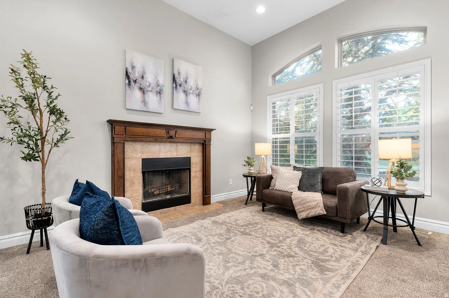 Living area featuring a floor-to-ceiling tiled fireplace with a wood mantel, high ceilings, recessed lighting, and multiple windows with plantation shutters