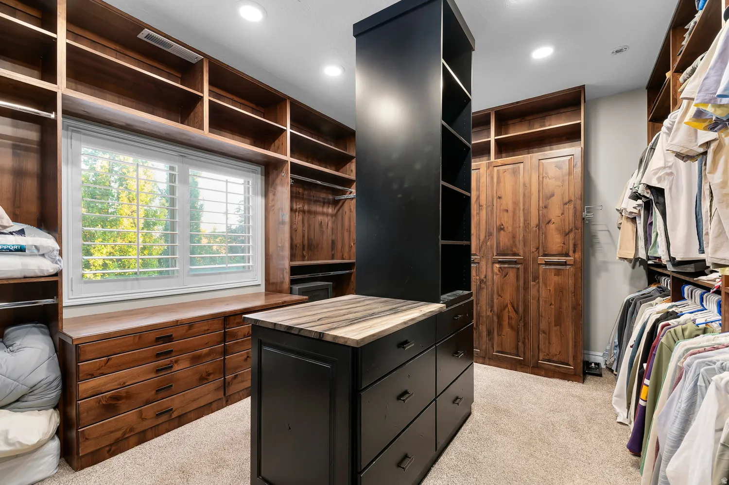 Custom walk-in closet featuring extensive built-in shelving, wood-finish cabinetry, and a central island with a stone countertop