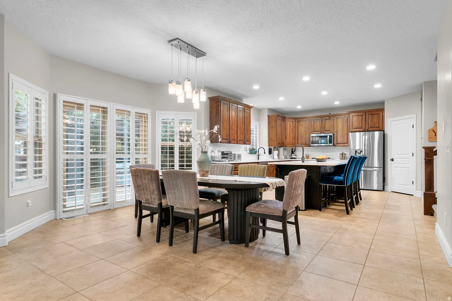 Open-concept kitchen and dining area featuring tile flooring, a multi-paneled glass door with plantation shutters, recessed lighting, and a kitchen island with seating