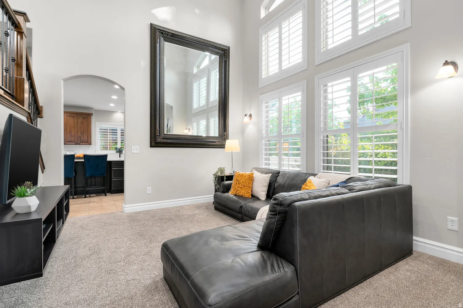 Living space featuring soaring ceilings, a grand mirror accent, and tall windows with white plantation shutters