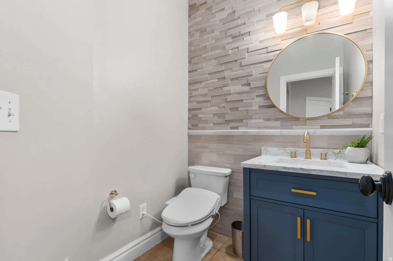 Powder room featuring a blue vanity with gold hardware, a white countertop, and a gold-framed circular mirror