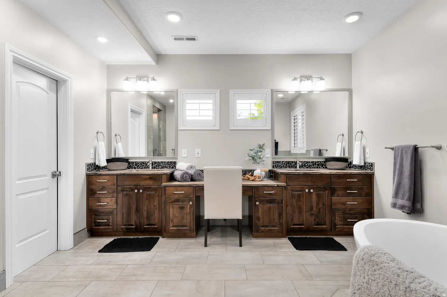 Bathroom featuring dual vanity areas with wood cabinetry, stone countertops, and individual mirrors with sconce lighting