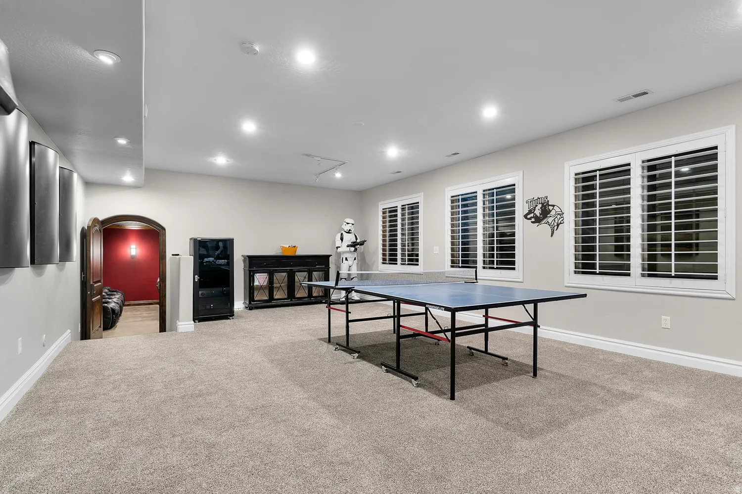 Spacious recreation area featuring plush carpet flooring, recessed lighting, and multiple windows with plantation shutters