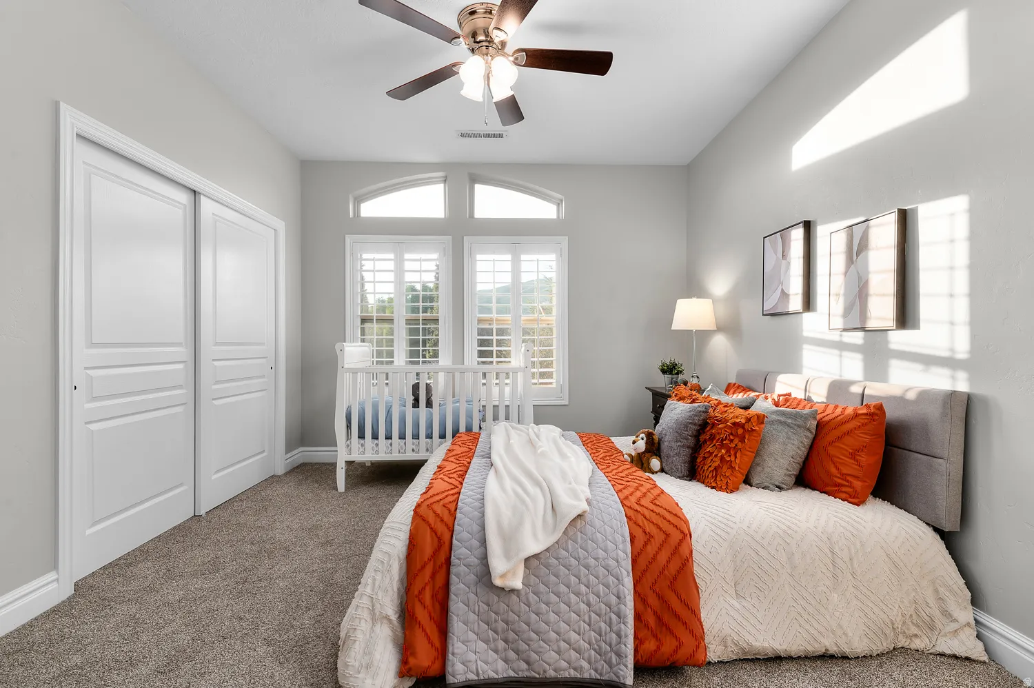 Carpeted bedroom featuring a ceiling fan with integrated lighting, a dual-pane window with arched transom, plantation shutters, and a sliding door closet