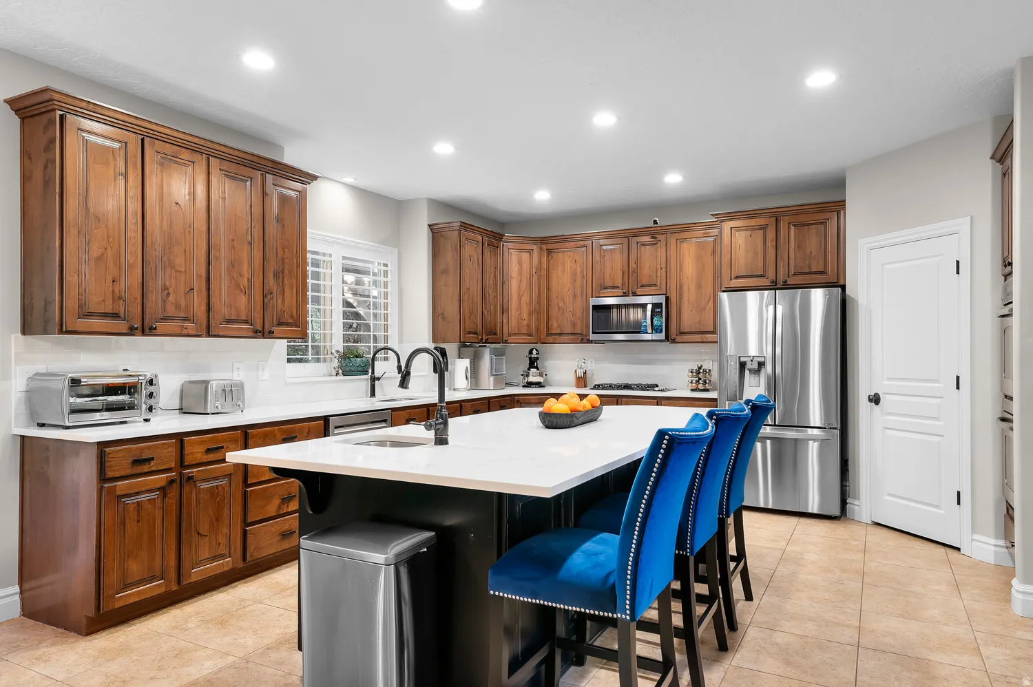 Spacious kitchen featuring warm wood cabinetry, white countertops, a large island with an integrated sink, stainless steel appliances, and recessed lighting