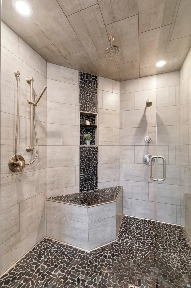 Spacious walk-in shower featuring pebble stone flooring and a built-in bench