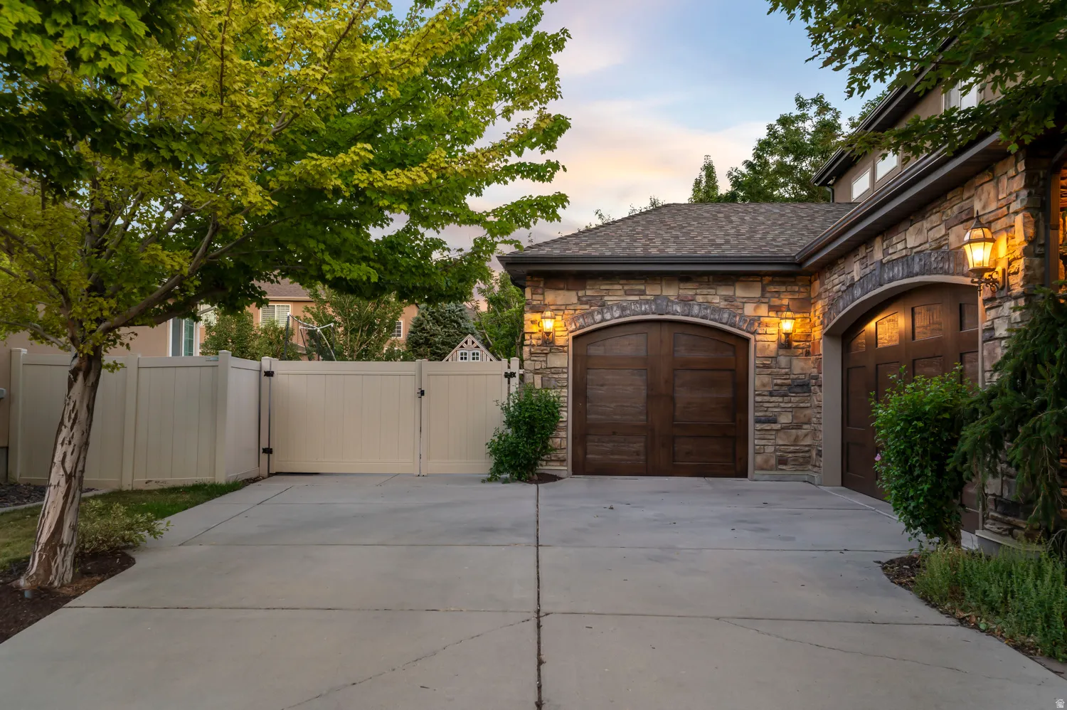 Stone facade with arched wood-finish garage doors, accented by exterior sconce lighting