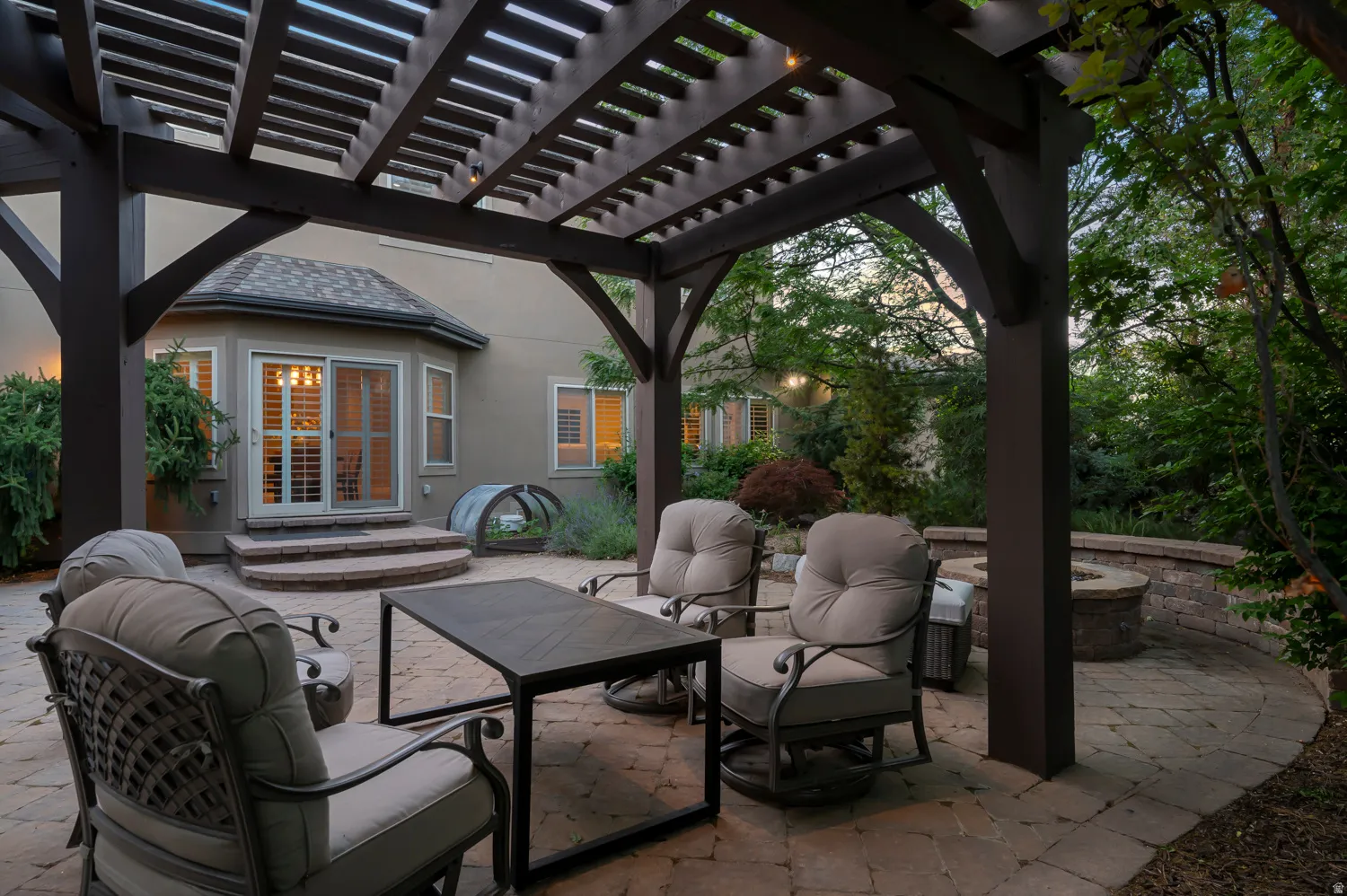 Expansive paver patio featuring a dark wood pergola with exposed beams