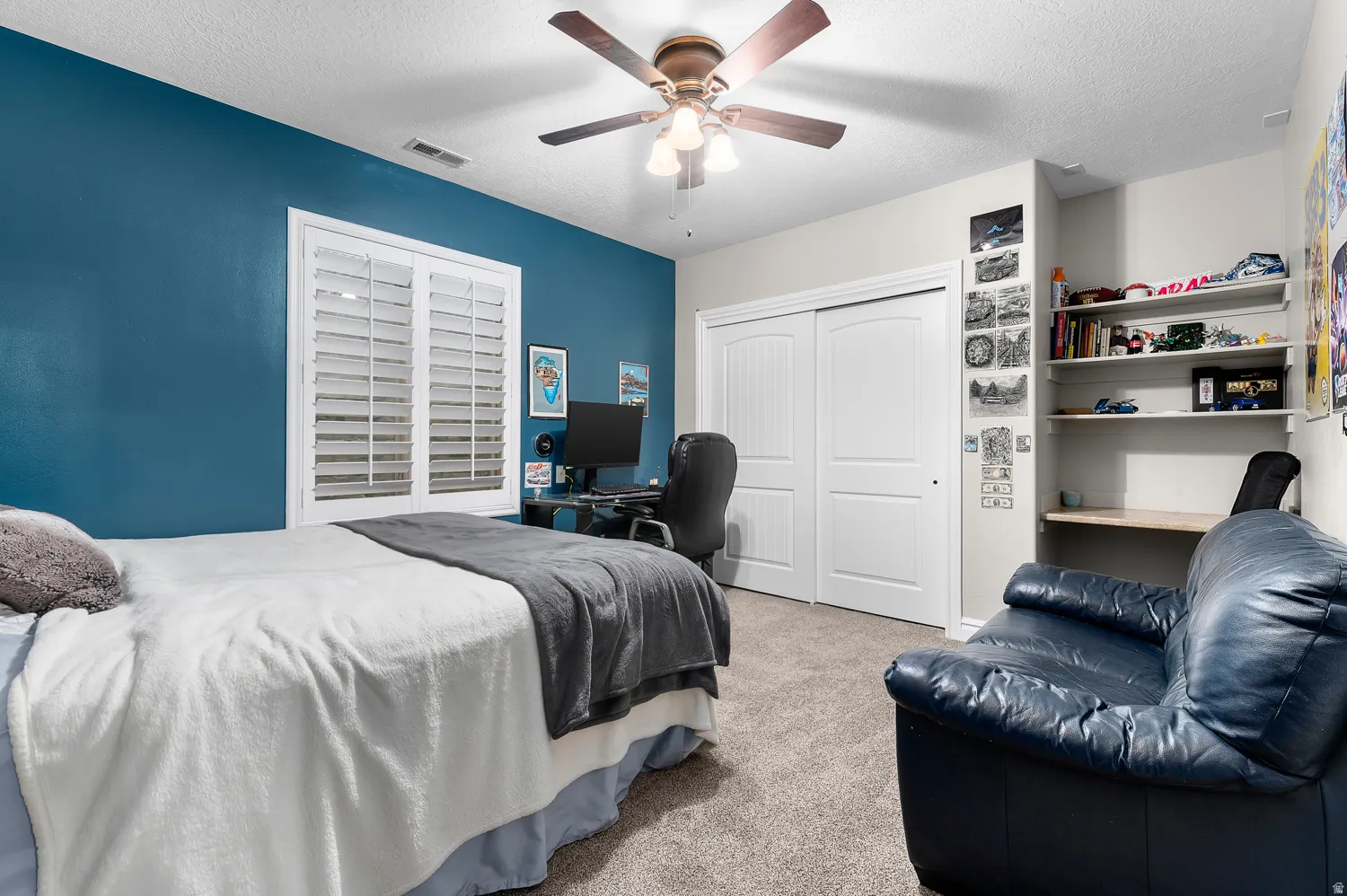 Carpeted room featuring a ceiling fan, built-in shelving, white sliding closet doors, and a window with white plantation shutters
